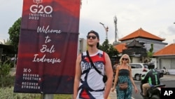 FILE - Tourists walk past a G20 banner in Nusa Dua, Bali, Indonesia on Friday, Nov. 11, 2022. The tropical island's ailing tourism industry returned after a two-year closure due to the pandemic. (AP Photo/Firdia Lisnawati)