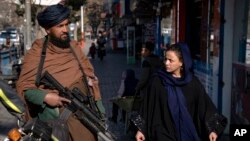 A Taliban fighter stands guard as a woman walks past in Kabul, Afghanistan, on Dec. 26, 2022. 