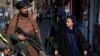 Arhiv - Talibanski borac na straži dok pored njega prolazi žena, u Kabulu, Afganistana, 26. decembra 2022.