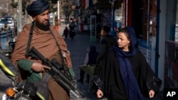 FILE - A Taliban fighter stands guard as a woman walks past in Kabul, Afghanistan, Dec. 26, 2022. 