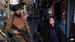 A Taliban fighter stands guard as a woman walks past in Kabul, Afghanistan, on Dec. 26, 2022. 