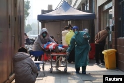 Seorang pekerja medis memindahkan tempat tidur rumah sakit yang membawa seseorang, di luar klinik demam rumah sakit, setelah pemerintah melonggarkan pengendalian penyakit COVID-19 di Wuhan, provinsi Hubei, China, 10 Desember 2022. REUTERS/Martin Pollard