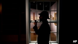 FILE - Curator Timothy Long is silhouetted as he poses for photographers with a Sherlock Holmes style pipe and deerstalker hat to promote an exhibition about the famed detective at the Museum of London, Oct. 16, 2014. 