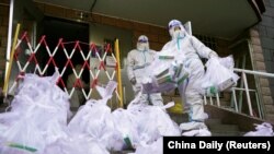 身穿防护服的工作人员给北京朝阳区一个被封控的居民楼发放新冠核酸检测盒。（2022年11月21日）