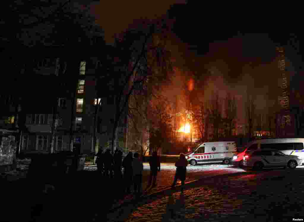 Locals gather near a building as a critical power infrastructure burns after a Russian drone attack in Kyiv, Ukraine.
