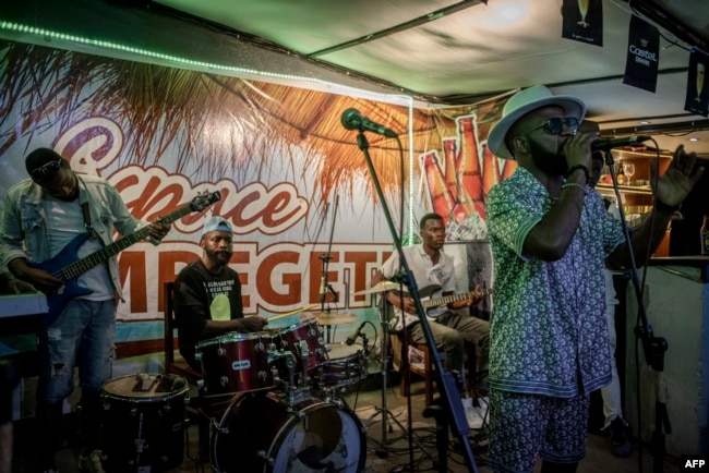 FILE - JC Kibombo (R), a renowned musician, sings with his musical band on a bar's podium in front of an audience dancing to his music in Goma, eastern Democratic Republic of Congo on November 20, 2022. (Photo by Guerchom Ndebo / AFP).