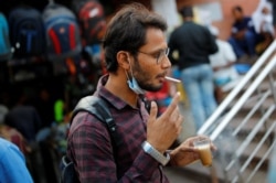 Seorang pria yang memakai masker pelindung wajah merokok di tengah penyebaran COVID-19 di kawasan tua Delhi, India, 20 Oktober 2020. (Foto: REUTERS/Adnan Abidi)