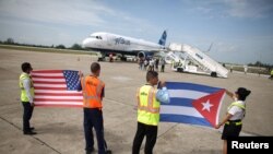 El personal de tierra sostiene banderas de EEUU y Cuba en el aeropuerto de Santa Clara, al centro de la isla, cerca de un avión de JetBlue, el 31 de agosto de 2016.