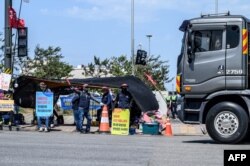 Pengemudi truk Korea Selatan yang sedang melakukan aksi mogok memberi isyarat kepada pengemudi truk lainnya di luar pelabuhan peti kemas di Incheon, 14 Juni 2022, pada hari kedelapan protes atas kenaikan biaya bahan bakar yang semakin menggerogoti rantai pasokan global. (Foto: ANTHONY WALLACE / AFP)