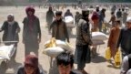 Un combatiente del Talibán vigila mientras varias personas reciben raciones de comida distribuidas por un grupo de ayuda humanitaria de China, en Kabul, Afganistán, el sábado 30 de abril de 2022. 