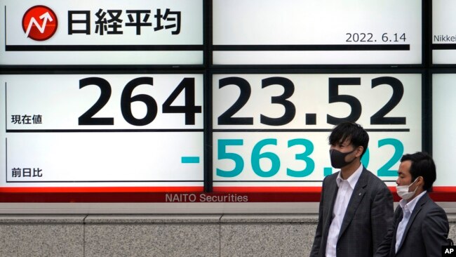 Men wearing masks walk past an electronic stock board showing Japan's Nikkei 225 index Tuesday, June 14, 2022, in Tokyo. Asian shares fell Tuesday after Wall Street tumbled into a bear market. (AP Photo/Shuji Kajiyama)
