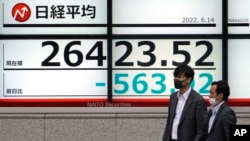 Men wearing masks walk past an electronic stock board showing Japan's Nikkei 225 index Tuesday, June 14, 2022, in Tokyo. Asian shares fell across the board Tuesday after Wall Street tumbled into a bear market.