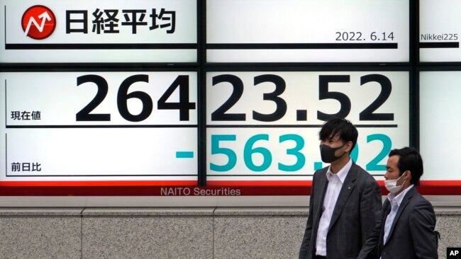 Men wearing masks walk past an electronic stock board showing Japan's Nikkei 225 index Tuesday, June 14, 2022, in Tokyo. Asian shares fell across the board Tuesday after Wall Street tumbled into a bear market.