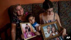 Danmara Triana, left, with her daughters Alice, center, and Claudia, show photos of them with their brother and father who moved to the United States in 2015, at their home in Cienfuegos, Cuba, Thursday, May 19, 2022. (AP Photo/Ramon Espinosa)