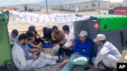 This image provided by Muhammad Arif Sarwari, shows Afghans who fled the Taliban takeover of their country checking their phones at Camp Bondsteel in Kosovo, June 1, 2022. 