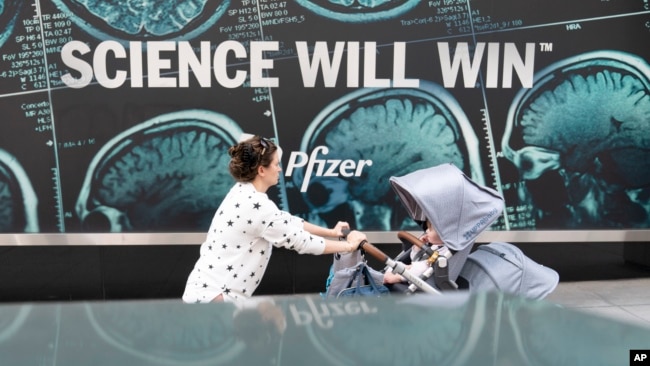 A woman pushes a baby in a stroller past a sign hanging outside Pfizer headquarters in New York, Monday, May 23, 2022. American health officials said Sunday that Pfizer's COVID-19 vaccine appears to be safe and effective for children under 5. (AP Photo/Mary Altaffer)