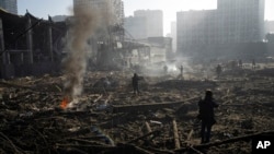 FILE - People survey the destruction amid the smoldering remains of a shopping center in Kyiv, Ukraine, following a shelling by Russian forces on March 21, 2022.