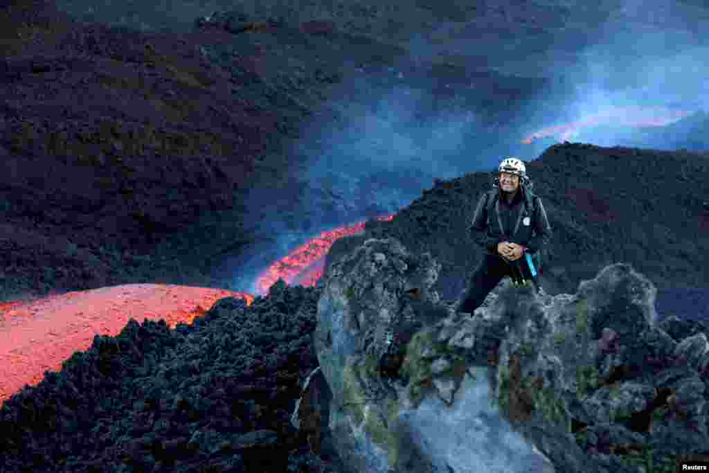 Seorang pendaki berpose dengan latar belakang aliran panjang lava merah panas yang mengalir di kawah tenggara Gunung Etna, gunung berapi tertinggi dan paling aktif di Eropa, terlihat dari Zafferana Etnea, Italia (11/6) (Foto: Reuters).&nbsp;