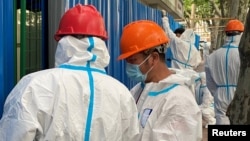 FILE - Workers in protective suits set up barriers outside a building, following the coronavirus disease (COVID-19) outbreak, in Shanghai, China, June 9, 2022.