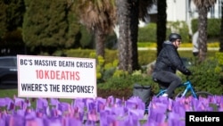 FILE - A cyclist rides past hundreds of flags symbolizing the more than 10,000 people who have died of toxic drug overdoses in British Columbia, Canada during a demonstration by the drug user advocacy group Moms Stop The Harm in Vancouver, Canada April 14, 2022.