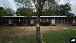 FILE -A school building stands behind a tree with an American flag and crime scene tape at Robb Elementary School in Uvalde, Texas, May 30, 2022. 