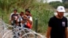 Migrants walk past razor wire fencing to be taken by the Border Patrol after crossing the Rio Grande river towards the U.S. in Eagle Pass, Texas, May 22, 2022. 