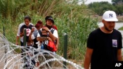 Migrants walk past razor wire fencing to be taken by the Border Patrol after crossing the Rio Grande river towards the U.S. in Eagle Pass, Texas, May 22, 2022. 