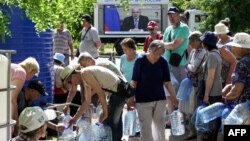 Local residents get water as Russian Prime Minister Mikhail Mishustin appears on a screen in the city of Mariupol on June 3, 2022.