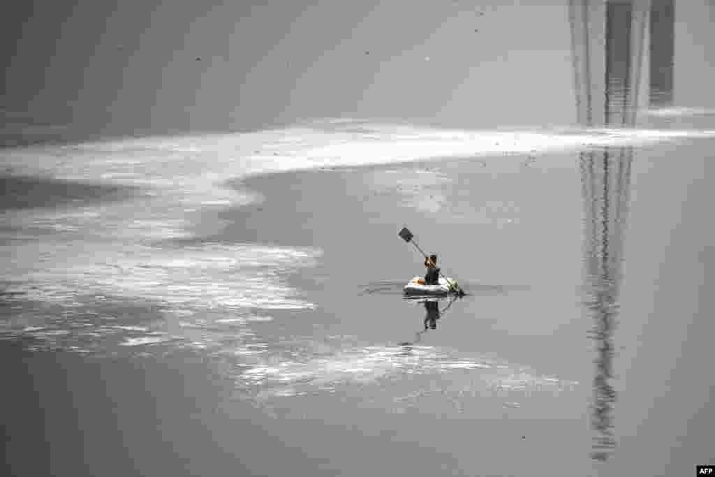 A boy rows a boat across the polluted waters of River Yamuna laden with foam, on a hot summer day in New Delhi, India.