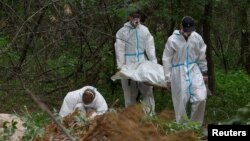 FILE - Forensic technicians carry the body of a person who, according to Ukrainian police, was killed and buried in an area ransacked by occupying Russian troops, near the village of Vorzel, Bucha district, Kyiv region, Ukraine June 13, 2022.