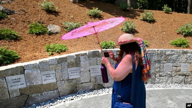 FILE - Karla Hailer, a fifth-grade teacher from Scituate, Massachusetts takes a video on July 19, 2017, where a memorial stands at the site where women were executed as witches. (AP Photo/Stephan Savoia, File)