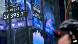 A cyclist wearing a protective mask stands in front of an electronic stock board showing Japan's Nikkei 225 index June 14, 2022, in Tokyo. Asian shares fell across the board Tuesday after Wall Street tumbled into a bear market.