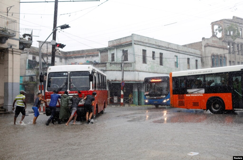 Menschen schieben bei starkem Regen in der kubanischen Hauptstadt einen Bus mit technischen Mängeln. | Bildquelle: VOA | Bilder sind in der Regel urheberrechtlich geschützt