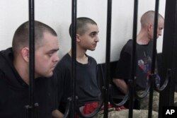 Two British citizens Aiden Aslin, left, and Shaun Pinner, right, and Moroccan Saaudun Brahim, center, sit behind bars in a courtroom in Donetsk, in the territory which is under the Government of the Donetsk People's Republic control, eastern Ukraine, June 9, 2022.