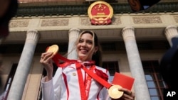 美国出生的中国奥林匹克队明星谷爱凌举着她在北京冬奥会上获得的三枚奖牌在北京人大会堂前拍照。（2022年4月8日）