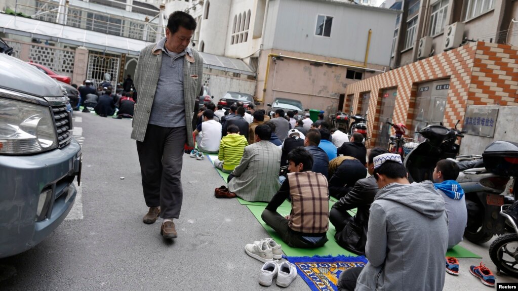 FILE - A Chinese man looks at Uighur people as they pray at a mosque in Shanghai, April 11, 2014.