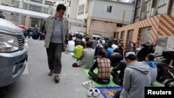 FILE - A Chinese man looks at Uighur people as they pray at a mosque in Shanghai, April 11, 2014.