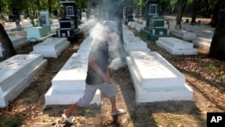 FILE - In this photo taken April 18, 2015, Nguyen Van Ba helps visitors place sticks of incense into graves at the former South Vietnamese military cemetery, in Binh Duong province, outside of Ho Chi Minh City, Vietnam.