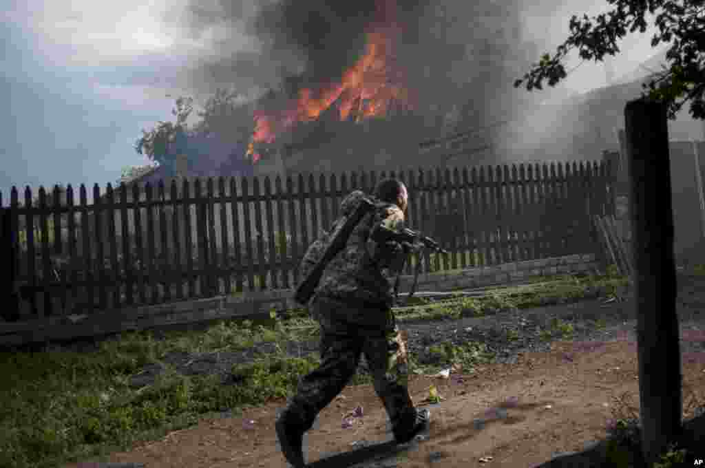 A pro-Russian armed man runs past a burning house after it was set on fire by a mortar shell, on the outskirts of the town of Lysychansk, Ukraine, May 22, 2014. 