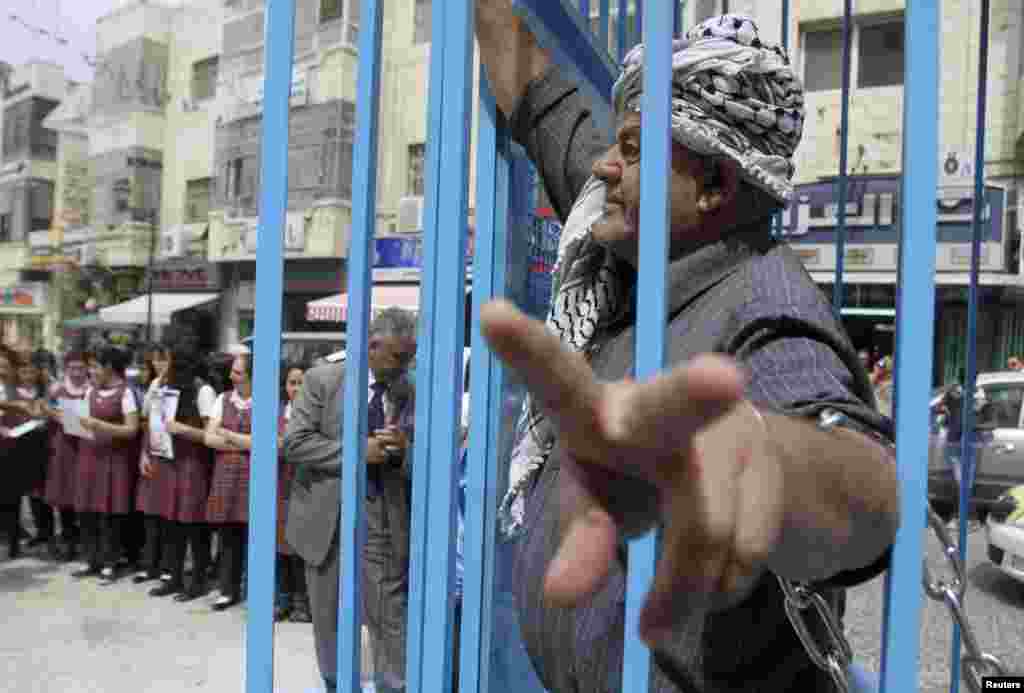 A Palestinian man gestures from inside a mock prison cell during a rally in the West Bank city of Ramallah, in support of Palestinian prisoners on a hunger strike in Israeli jails, May 14, 2012. 