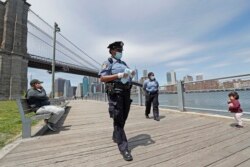 A youngster approaches a team of New York City police officers as they walk with face masks to hand out to anyone who needs or asks for one during the current coronavirus outbreak, Sunday, May 17, 2020, in Brooklyn Bridge Park in New York.