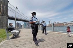 A youngster approaches a team of New York City police officers as they walk with face masks to hand out to anyone who needs or asks for one during the current coronavirus outbreak, Sunday, May 17, 2020, in Brooklyn Bridge Park in New York.