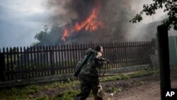 A pro-Russian armed man runs past a burning house after it was set on fire by a mortar shell, on the outskirts of the town of Lysychansk, Ukraine, May 22, 2014.