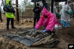 A forensic expert examines the body of a civilian during exhumation in the recently retaken area of Izium, Kharkiv region, Ukraine, Sept. 23, 2022.