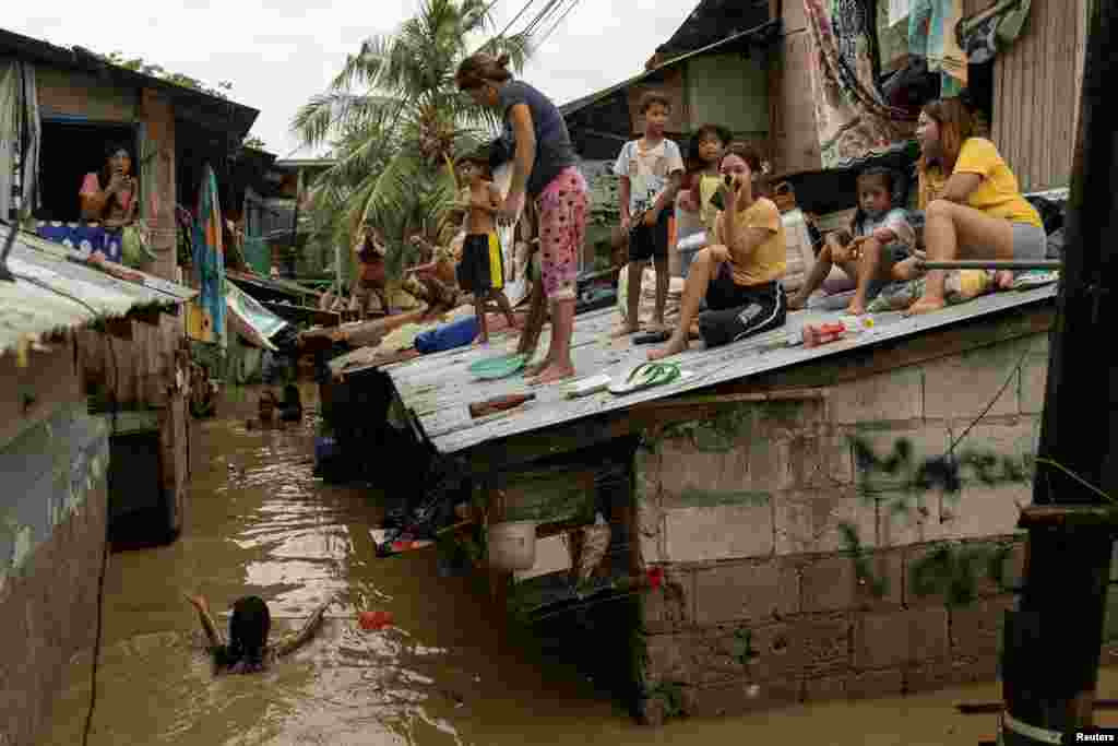 Residents wait on the roof of their homes for flooding to subside after Super Typhoon Noru, in San Miguel, Bulacan province, Philippines, Sept. 26, 2022.