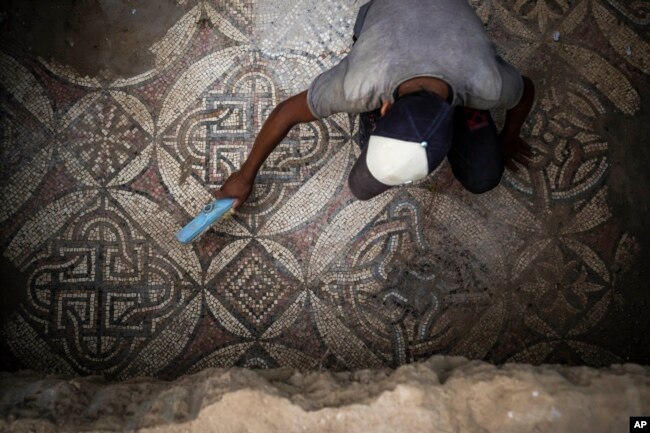 A Palestinian sweeps dust off parts of a Byzantine-era mosaic floor that was uncovered by a farmer in Bureij in central Gaza Strip, Sept. 5, 2022. . (AP Photo/Fatima Shbair)