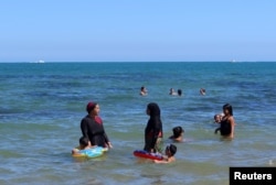 A woman, wearing a full-body burkini swimsuit, chats with another woman as they stand in the sea at a beach in La Marsa near Tunis, Tunisia September 11, 2022. (REUTERS/Jihed Abidellaoui)