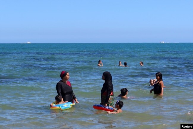 A woman, wearing a full-body burkini swimsuit, chats with another woman as they stand in the sea at a beach in La Marsa near Tunis, Tunisia September 11, 2022. (REUTERS/Jihed Abidellaoui)