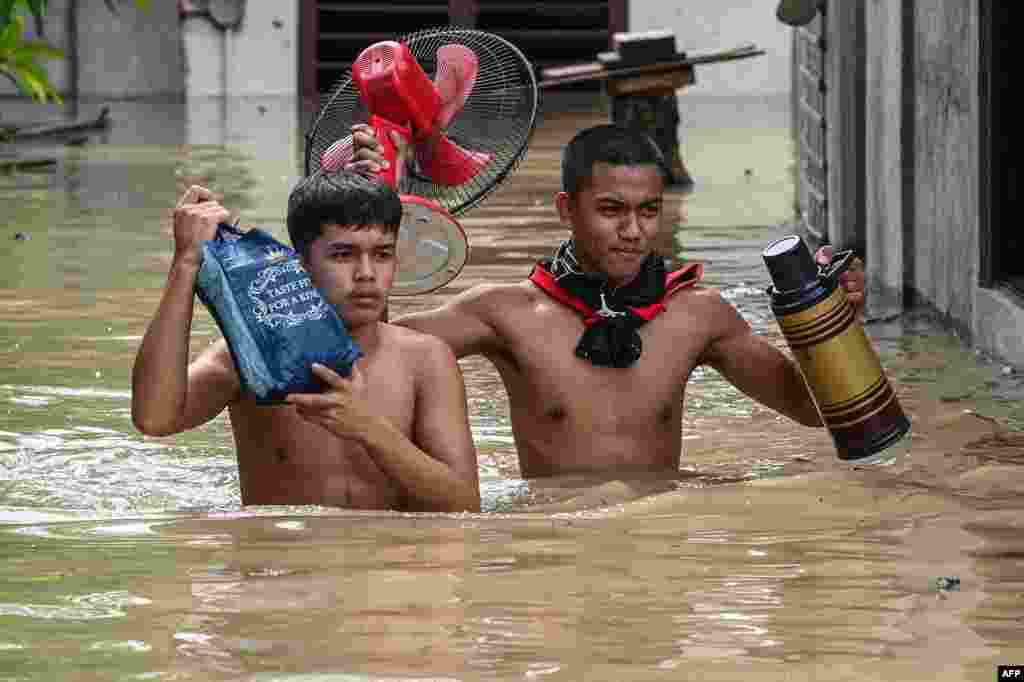 Residents carry their belongings while evacuating from their submerged homes in the aftermath of Super Typhoon Noru in San Ildefonso, Bulacan province on Sept. 26, 2022.