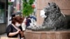 FILE - A shopper wearing a face mask checks her mobile phone beside a masked lion statue of a department store in Ginza shopping district in Tokyo, Aug. 30, 2022.